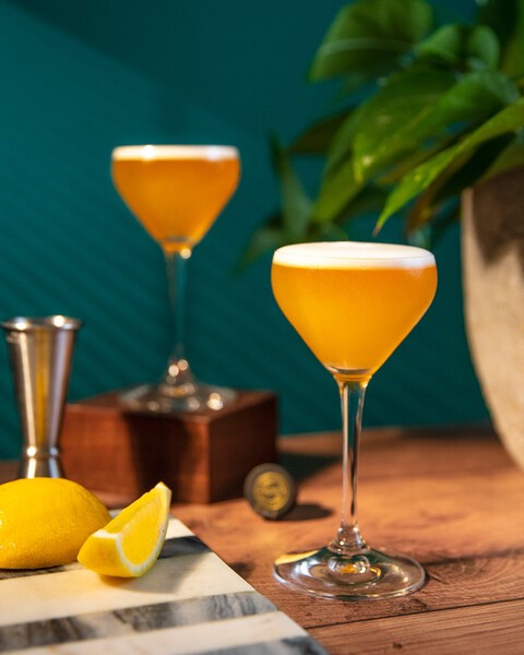 two whiskey sours served as brunch drinks alongside a slice of lemon
