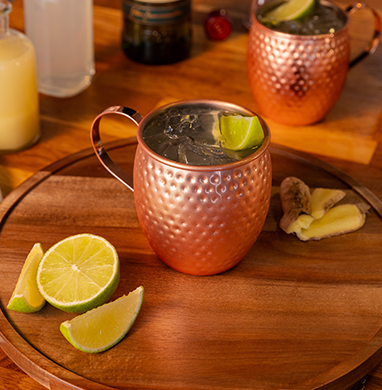 A refreshing Irish Mule cocktail served in a hammered copper mug with ice and lime wedges, accompanied by fresh ginger and citrus on a wooden tray, creating a warm and inviting bar setting.